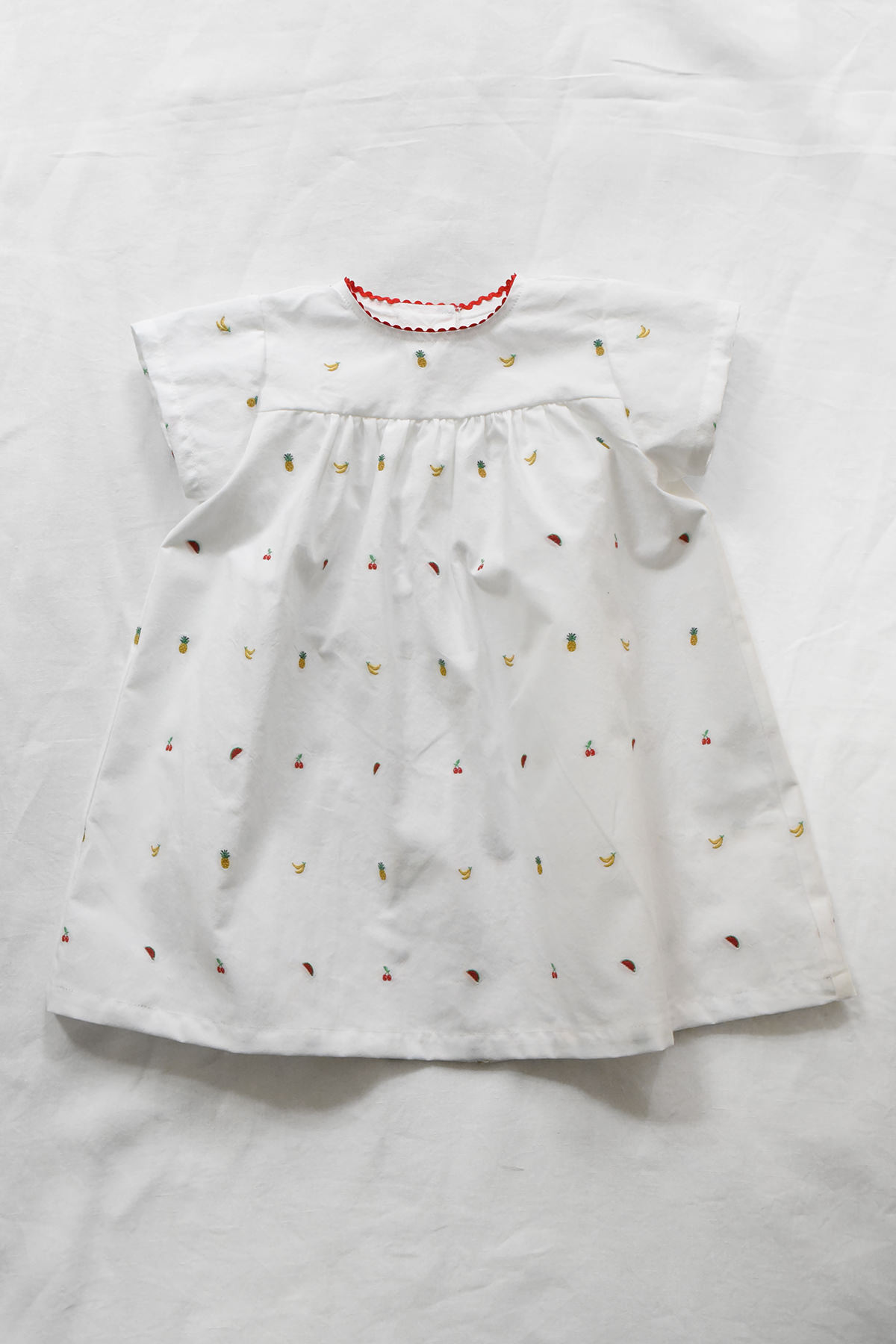 White dress in Italian fabric with embroidered fruit motifs, red ric rac trim at neckline and back button closure