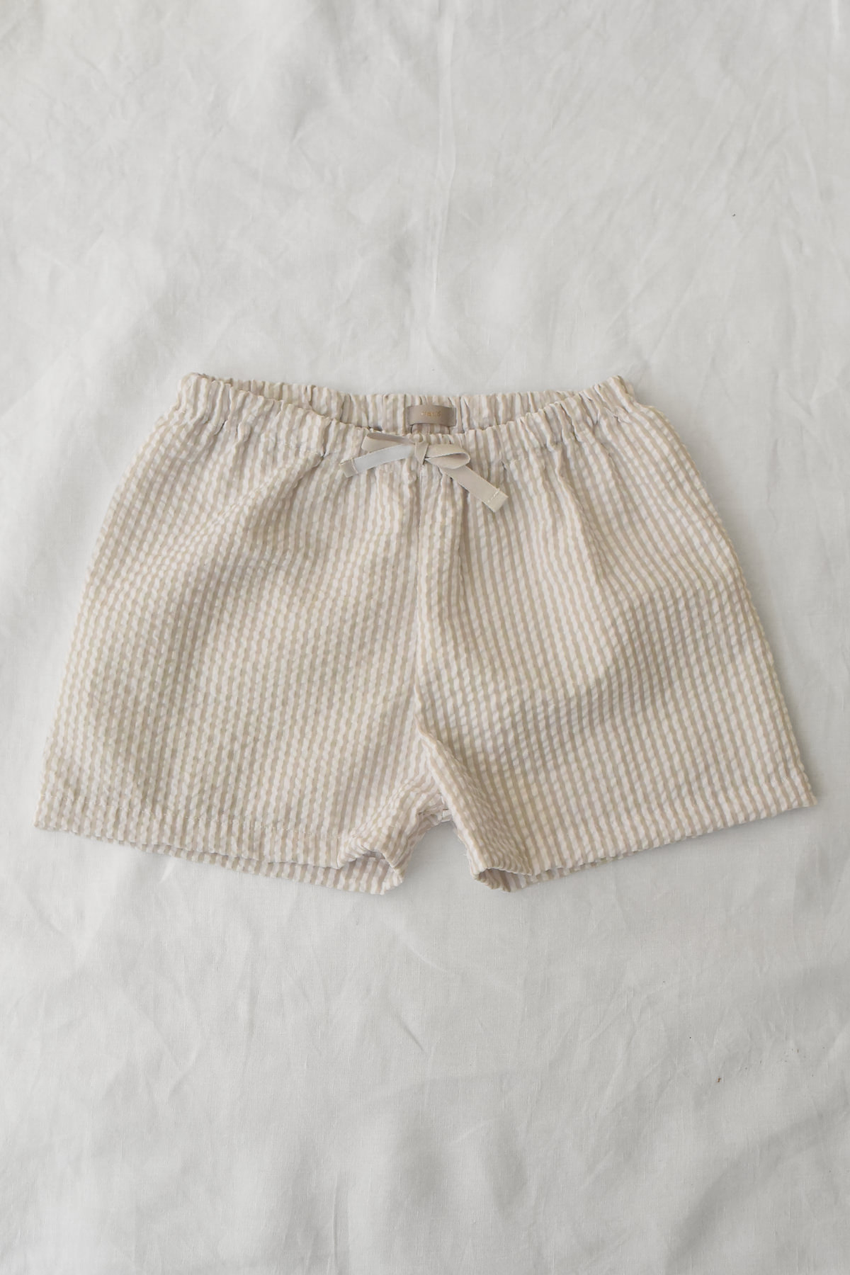 Lightweight beige and white striped shorts with elastic waistband and ribbon detail