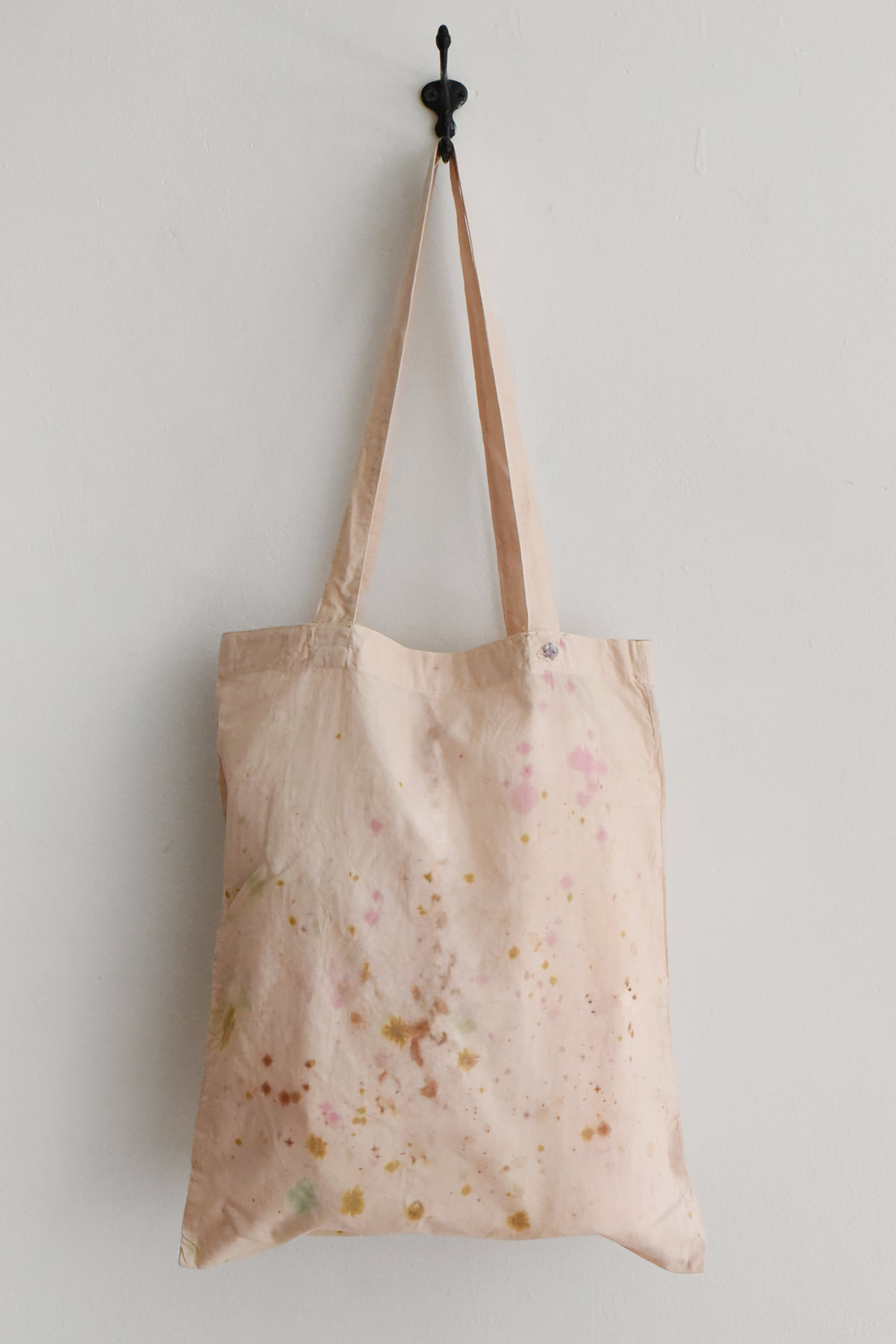 Hand-dyed and painted tote bag by Antonia Rossi with soft pink, yellow, and green splashes and a small embroidered detail on natural fabric.