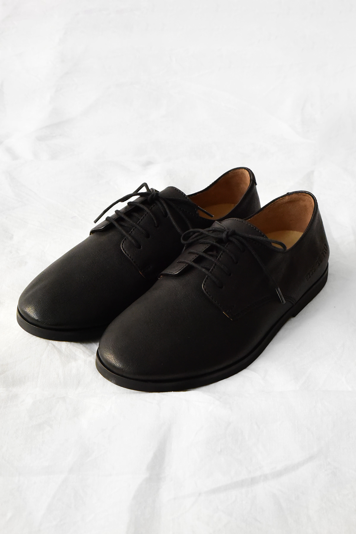 Common Projects Black leather derby shoes featuring a minimalist lace-up design and the iconic gold serial number on the outer heel.