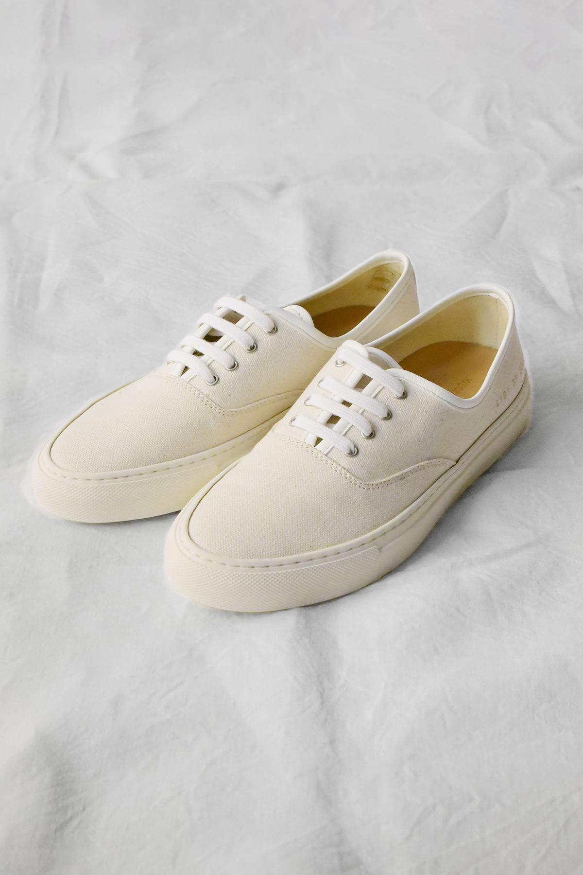 Common Projects 4-hole canvas slip-on in beige.