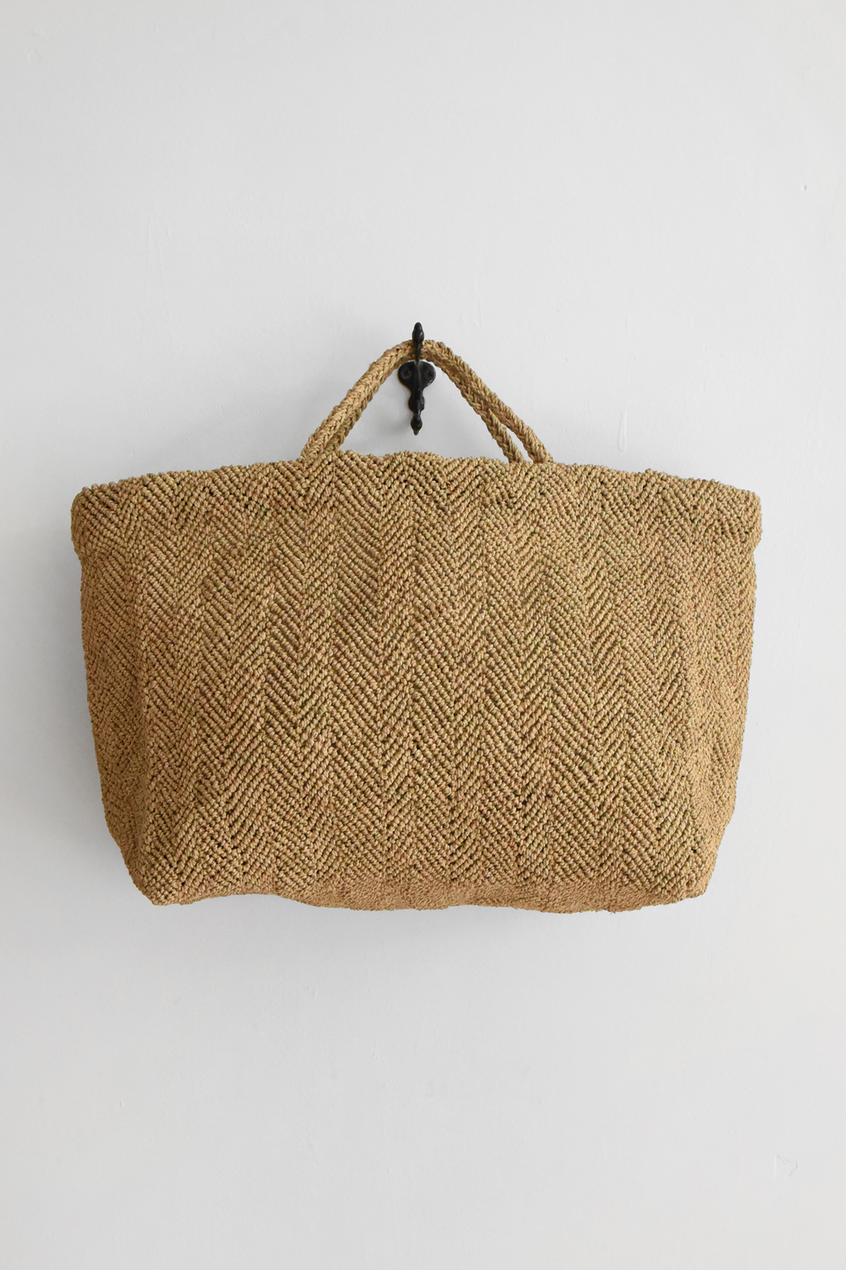 Hand crocheted raffia tote bag with chevron-like textured pattern, double handles, and wide structured shape