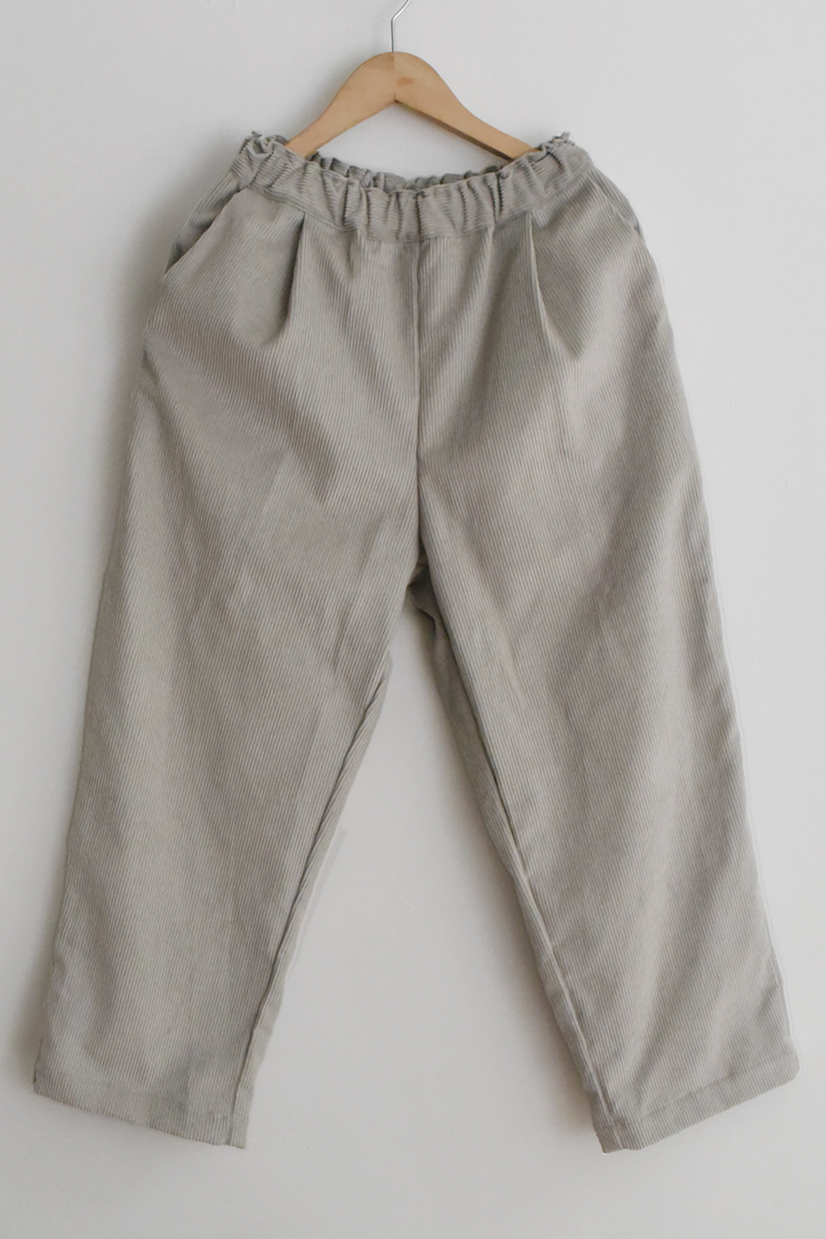 MAKIE Corduroy Straight Pants Skylar in Sand, featuring an elastic waistband and side pockets, displayed on a wooden hanger against a white wall.