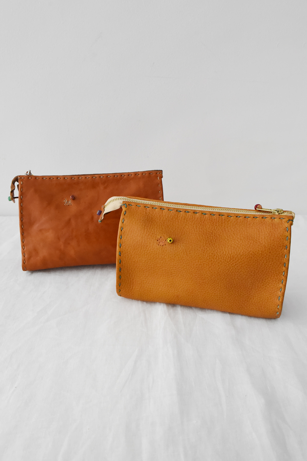 Two Henri, Pouch #046 leather zippered pouches with decorative whipstitching and small charms.