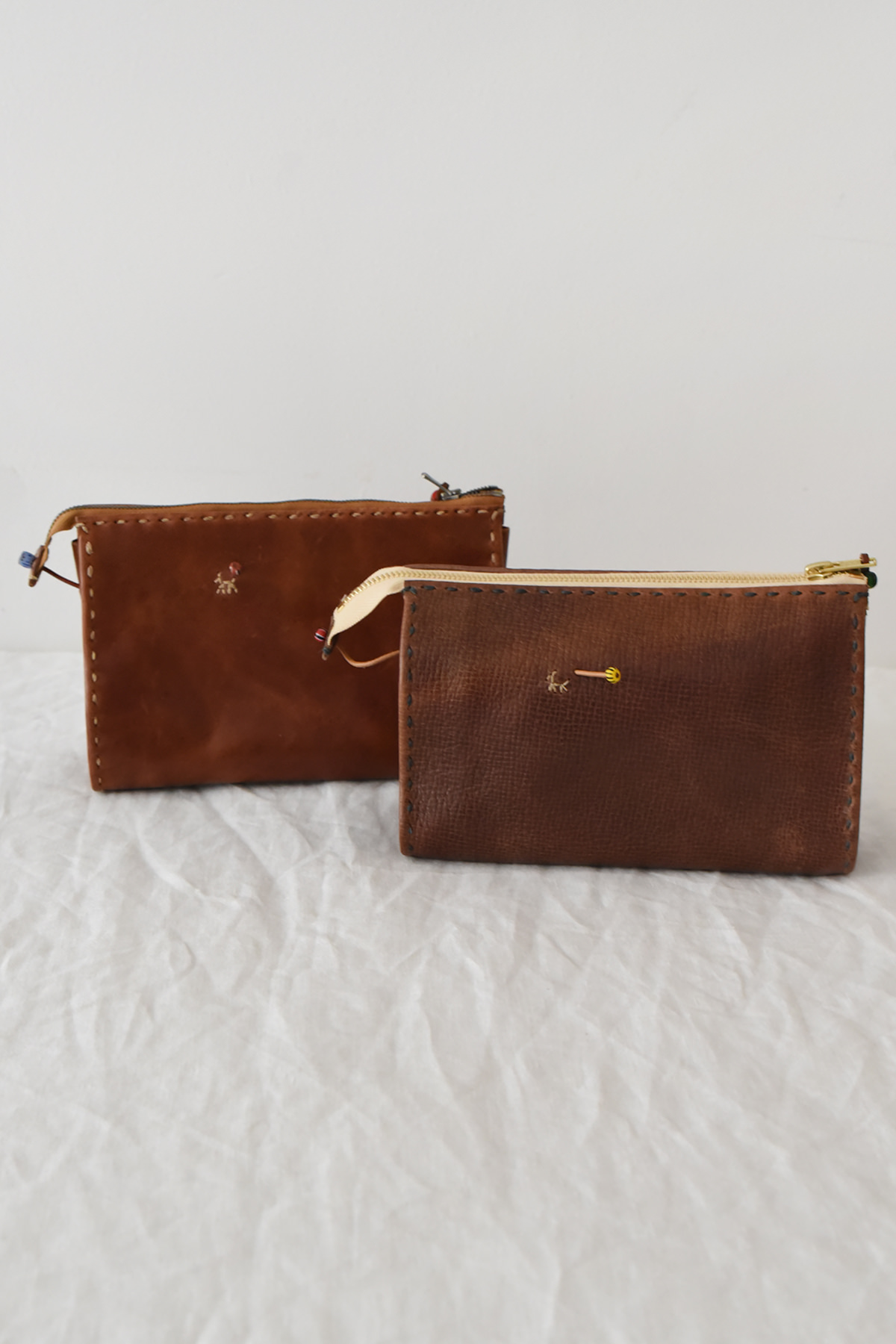 Two Henri, Pouch #047 brown leather zippered pouches with decorative stitching and small embroidered details.