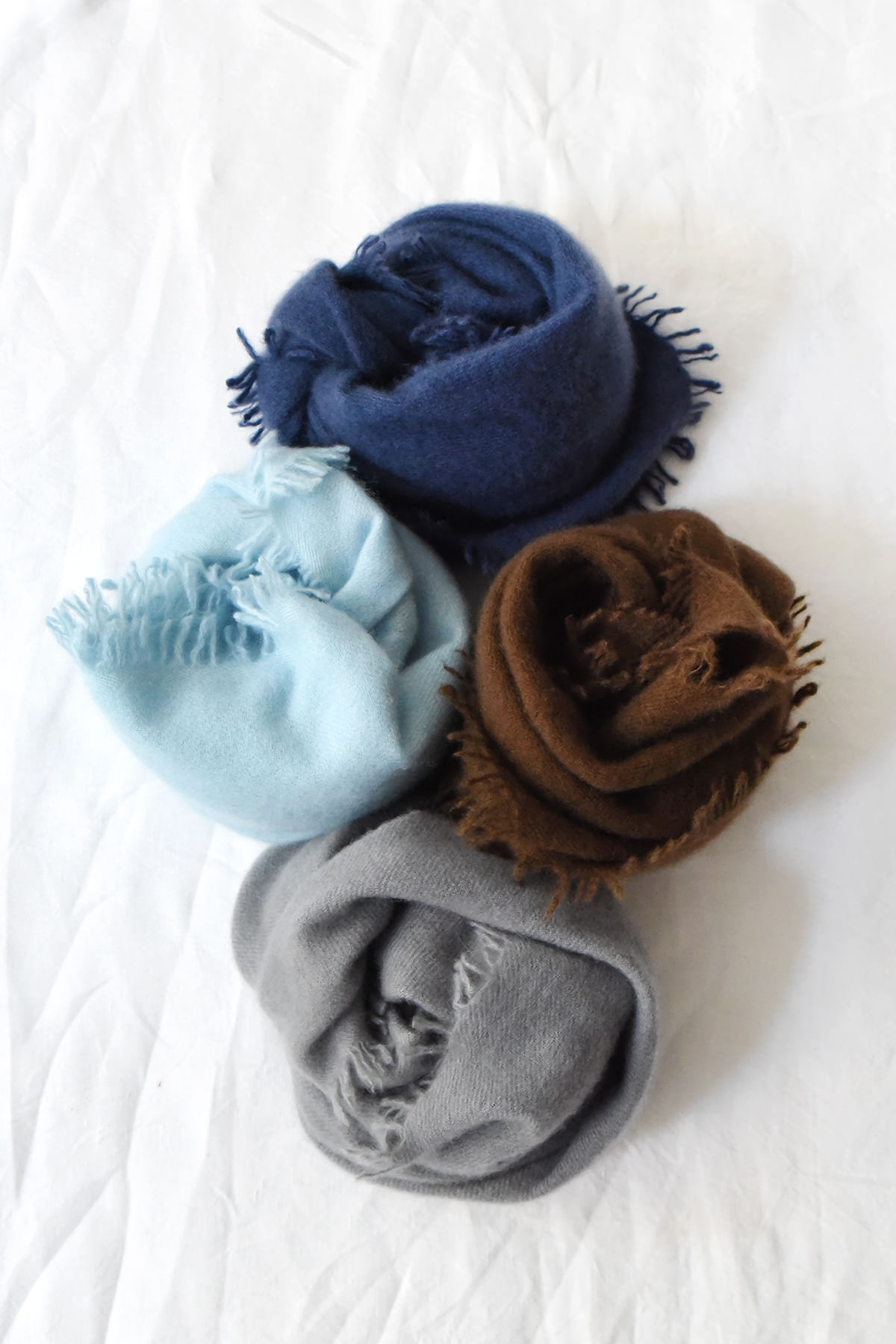 MAKIE, Cashmere Scarf Square 28x28 - No. 1: four square scarves with fringed edges in blue, light blue, brown, and gray, arranged in a cluster on a white surface.