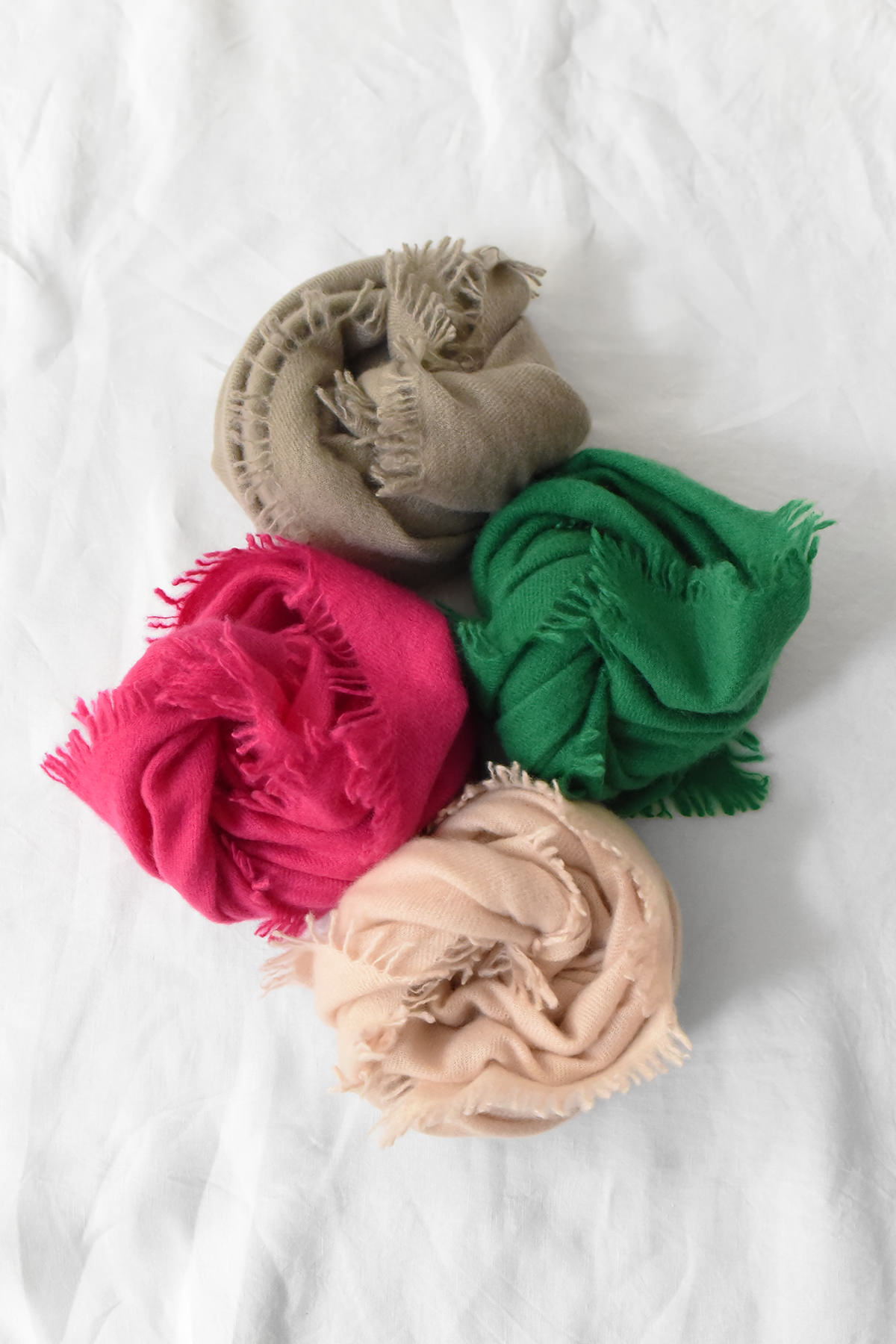 Four MAKIE, Cashmere Scarf Square 28x28 - No. 1 (Copy) scarves with fringed edges in tan, green, magenta, and beige, arranged in a cluster on a white surface.