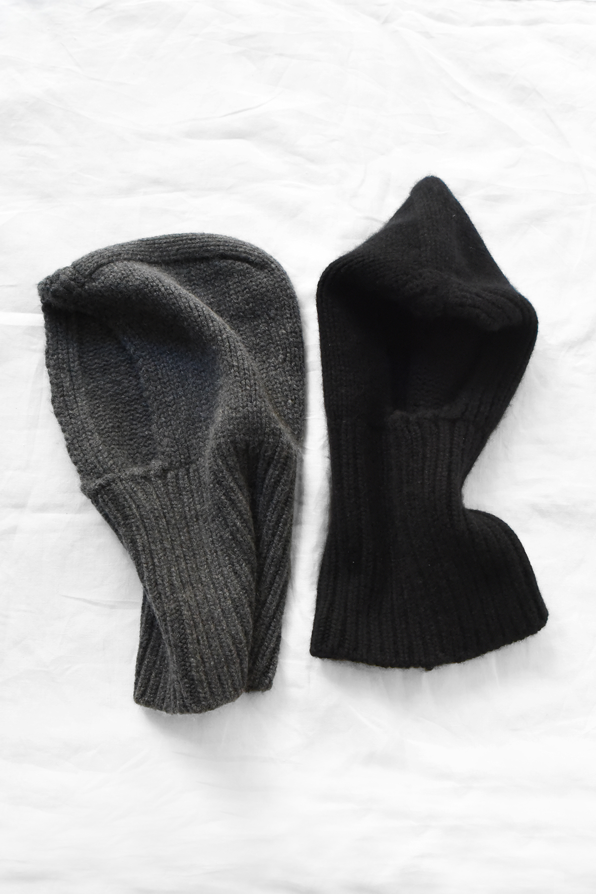 Two MAKIE, Cashmere Balaclavas, one charcoal gray and one black, laid flat on a white surface.