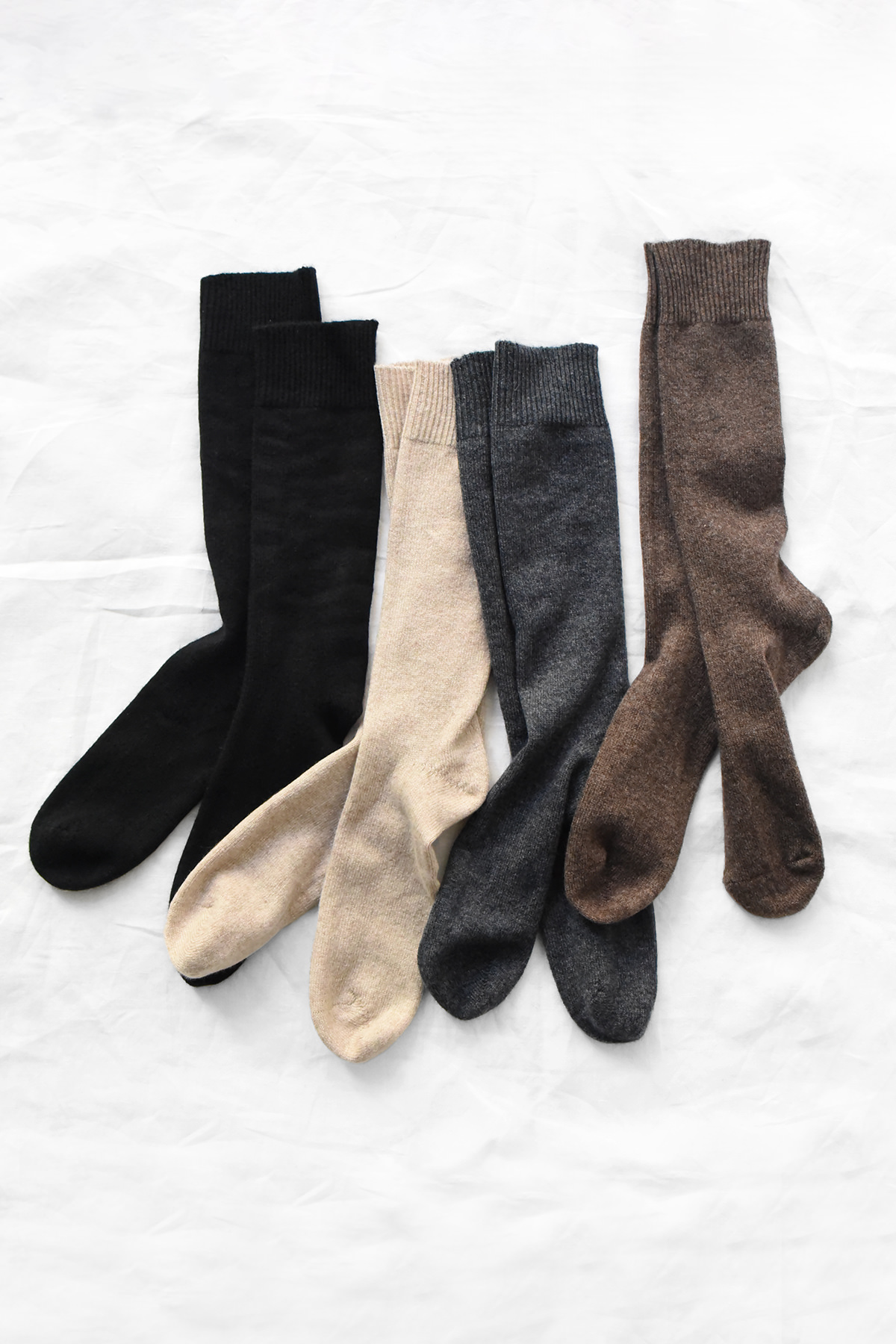 MAKIE 100% cashmere socks in Black, Natural, Charcoal, and Brown, with ribbed cuffs.