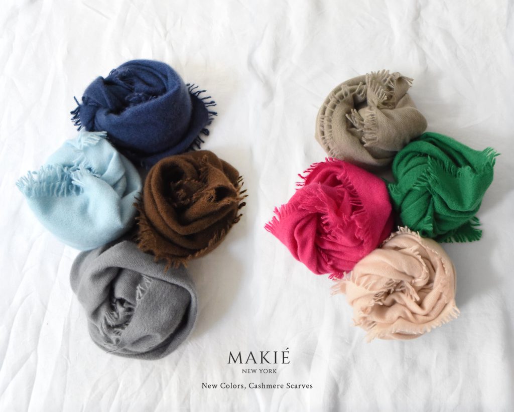 Eight rolled cashmere scarves in various colors arranged on a white surface, with text reading MAKIÉ NEW YORK New Colors, Cashmere Scarves.