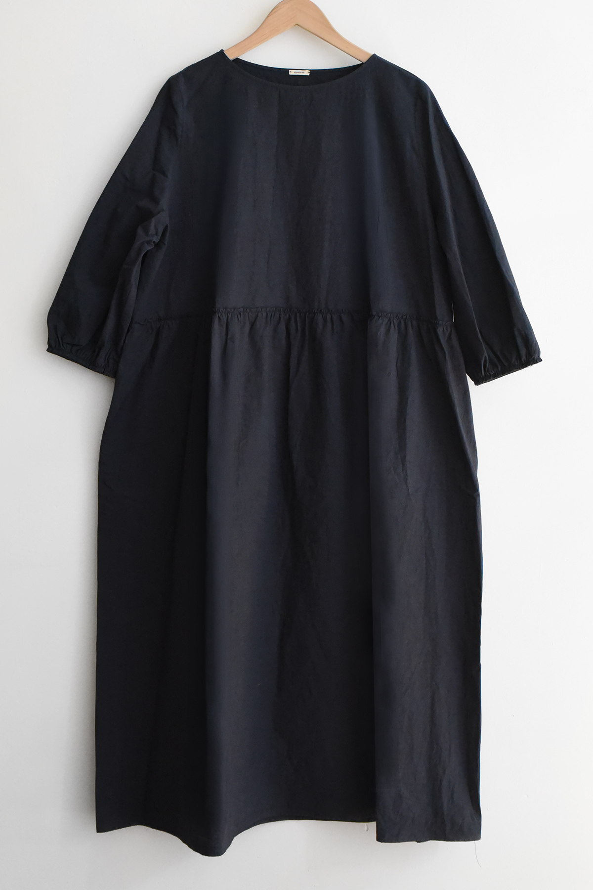 Apuntob (a.b) P2100 Dress in navy blue, featuring three-quarter length sleeves, a round neckline, and a gathered drop waist, hanging on a wooden hanger.