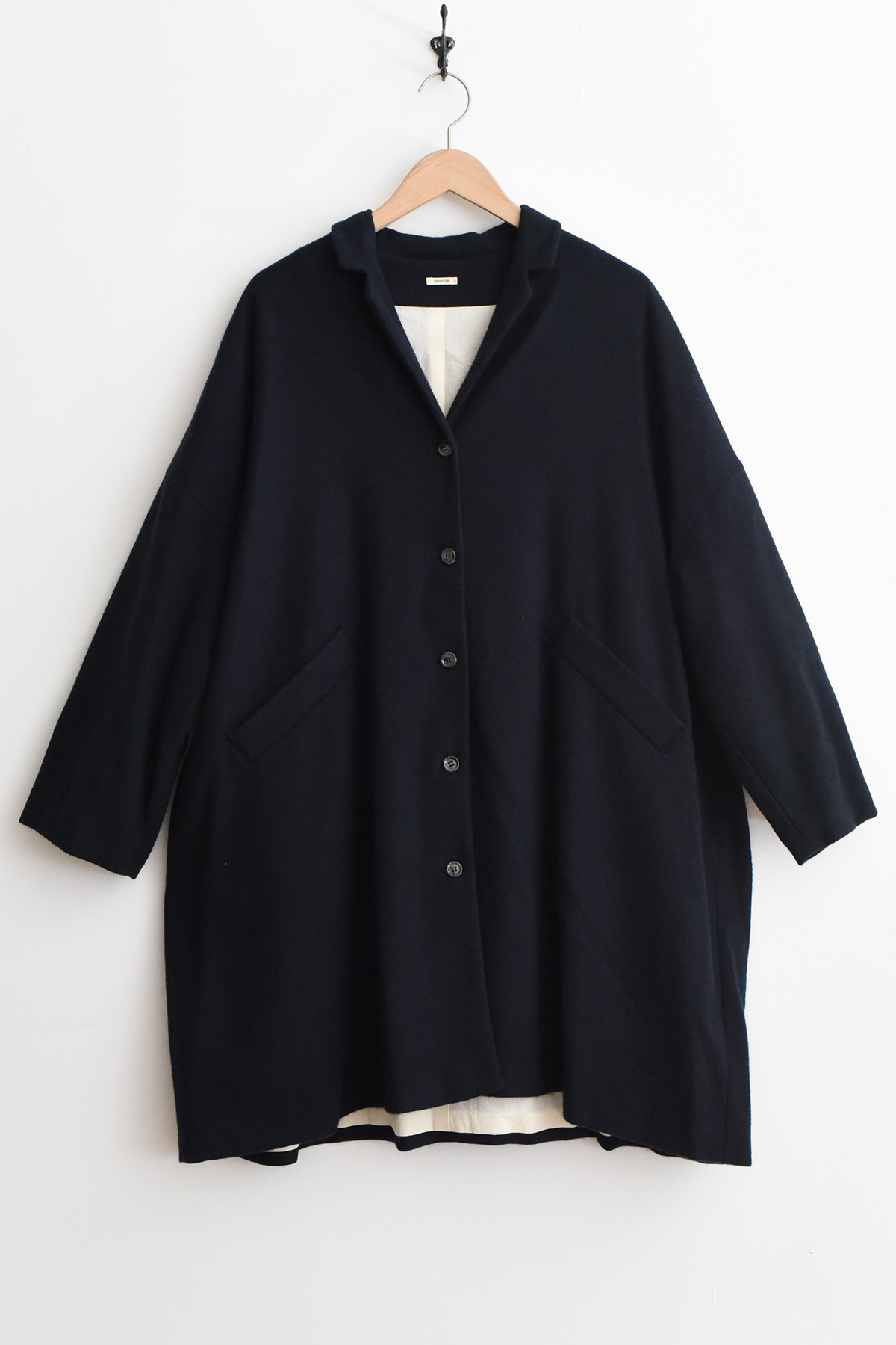 Navy apuntob (a.b) P2087 Coat with an open collar and slanted pockets, hanging on a wooden hanger against a white wall.
