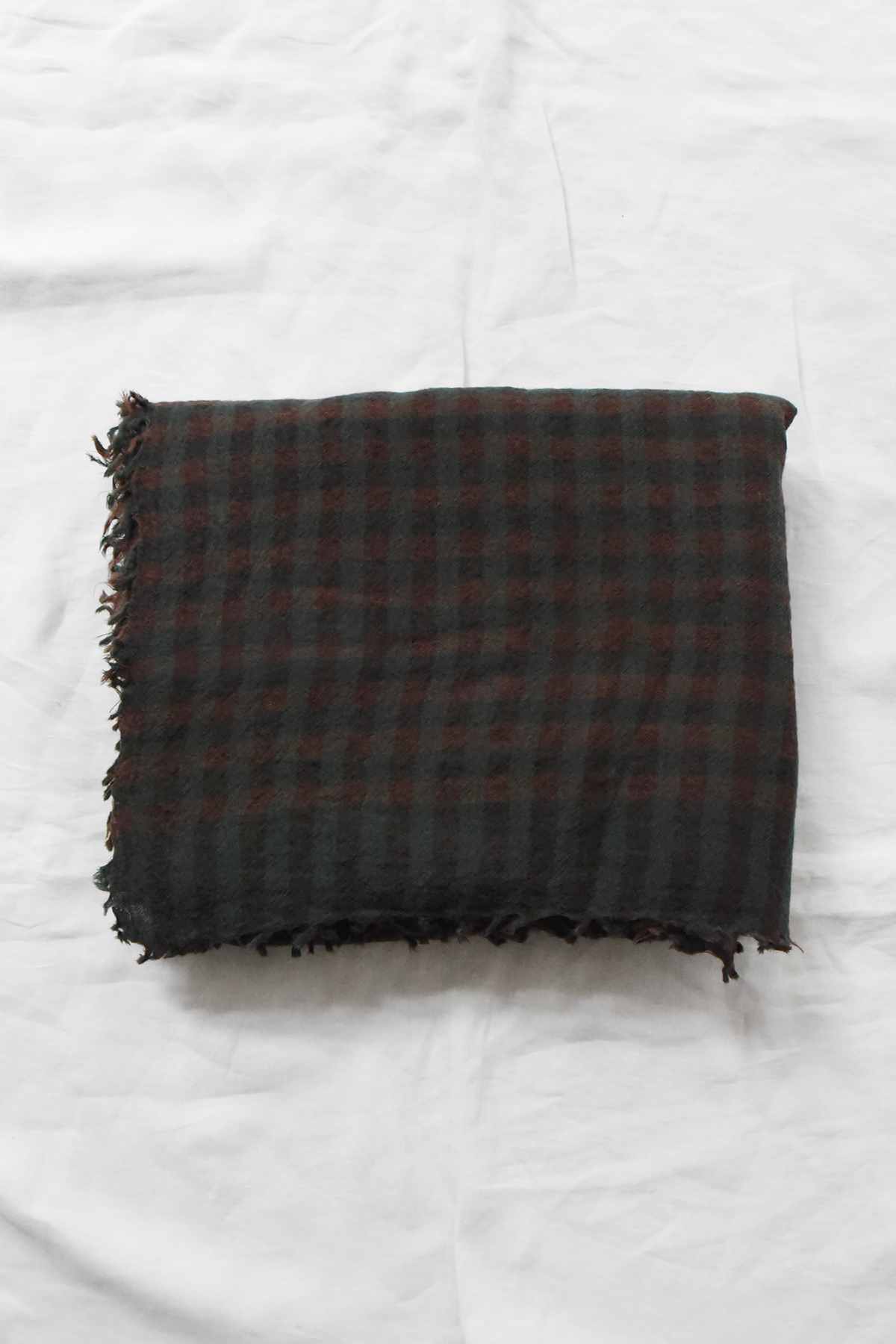 Manuelle Guibal, 7146 Wool Scarf YSH - Bottle in a dark green and brown checkered pattern with fringed edges, folded square on a white fabric surface.